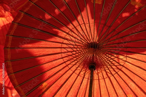 Close-up of an open, red, traditional parasol with light filtering through