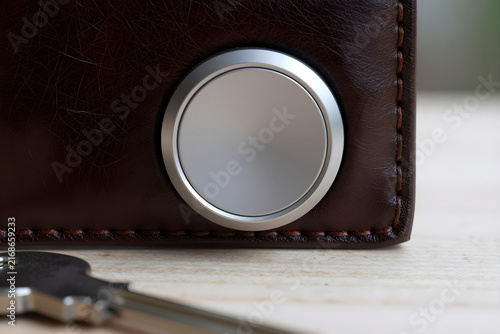 Extreme close-up of a matte aluminum smart tracker button resting on a leather wallet.