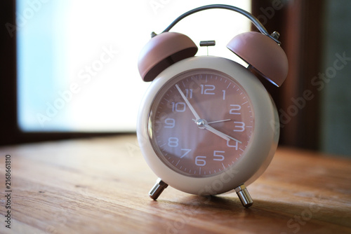 Bild auf Leinwand An alarm clock sits on a wooden table near a window, silhouetted against the light
