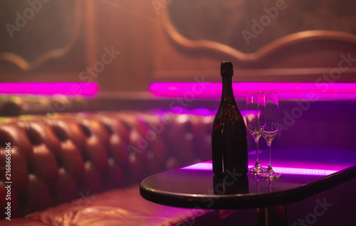 Champagne bottle and glasses in neon vip lounge.