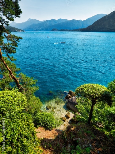 Scenic view of Lake Como from Villa del Balbianello gardens in Italy, with turquoise water, boats, lush greenery and Alpine mountains.