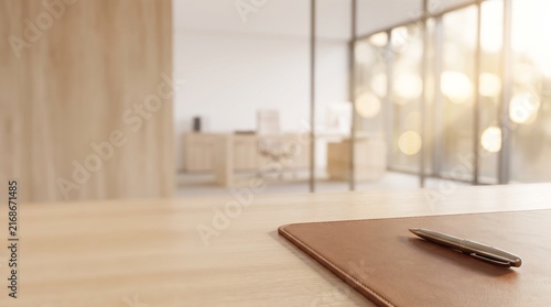 A close-up of a pen on a leather desk pad on a wooden table in a modern office with sunlight.