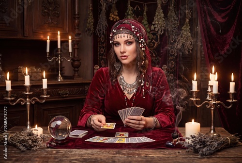 A mystical gypsy fortune teller reads tarot cards by candlelight inside a dark magical gothic room.