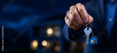 Real Estate Agent Holding House Key with Keychain at Night Concept of Home Ownership