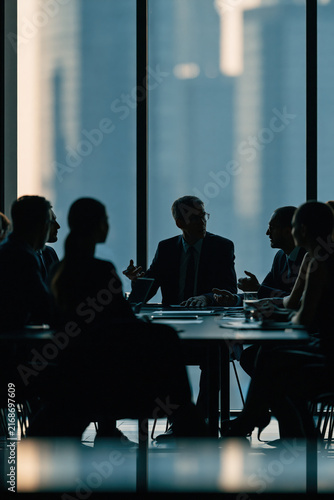business team silhouettes meeting in conference room, executives seated around table, vertical composition, photorealistic