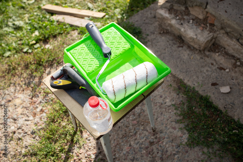 paint roller, tray and restoration tools prepared outdoors beside a house, showing equipment for repainting a metal entrance door during practical diy renovation