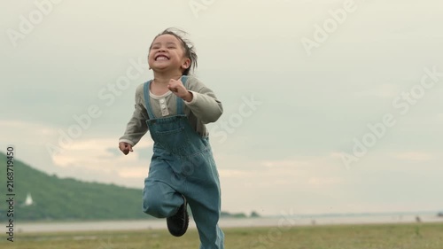 slow motion of happy preschool child girl running on a grass field near the river and mountain