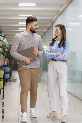 Colleagues walking and smiling in modern office, discussing business plans, professional teamwork collaboration