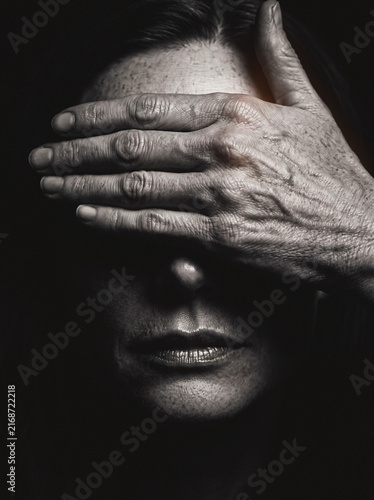 Hand covering man's eyes in dramatic monochrome close-up, mysterious moody portrait gesture