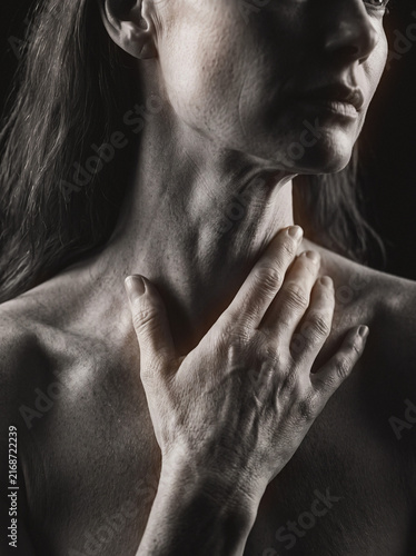 Woman touching neck with hand in dramatic monochrome close-up, sensual moody portrait gesture