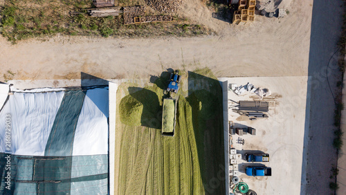 Aerial view of a tractor unloading and compacting freshly cut grass for silage on a farm with tire tracks visible on the ground in Mediglia, Lombardy, Italy.