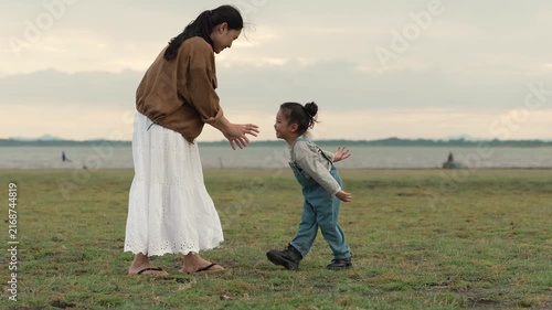 slow motion of joyful mother and daughter playing in an open field by the lake