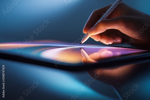 concept of creative freedom through technology. Gen Z. Close-up of hand using stylus on digital tablet screen with colorful light trails in dark environment