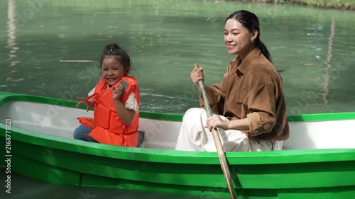 slow motion of happy mother and preschool child girl in a green paddle boat on a scenic pond.