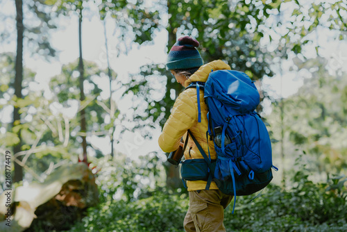 Female tourist with backpack hiking in mountain forest. Young asian woman wearing yellow puffer goose down jacket clothes for active lifestyle. Adventure at nature.