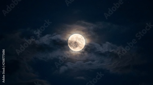 A bright full moon shining through thin dark clouds in the night sky during a clear evening