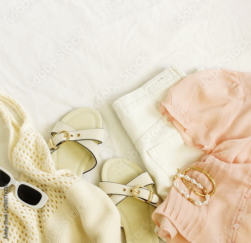 Flat lay of women's casual summer outfit pastel colors. Top view blouse, jeand, bag, sunglasses, shoes, bracelets on white linen background. Lifestyle .Space for text.