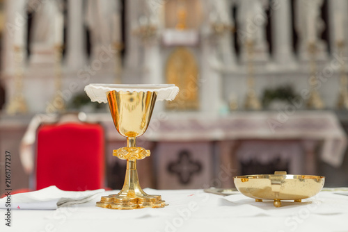 A holy mass takes place in a catholic church with an altar. A golden chalice and dish are prepared for the ceremony.