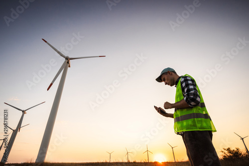 Wind Farm Worker Checking Smartphone Among Turbines at Sunset