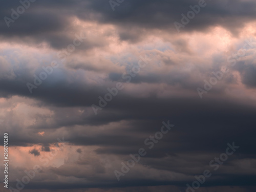 Dramatic dark storm clouds illuminated by warm sunset light, creating a moody cloudscape with layered rain clouds and an approaching thunderstorm atmosphere.