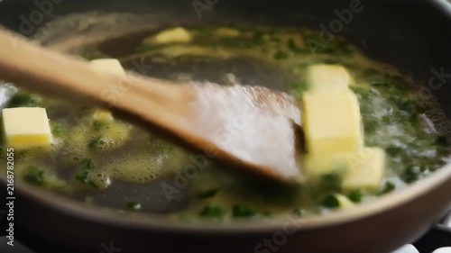 Melted butter mixing with herbs swirling in pan