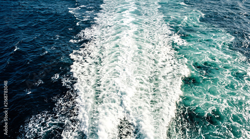 Ocean boat wake with white foam, deep blue sea water ripples, nautical ship trail in turquoise ocean, maritime travel background