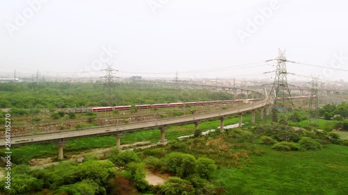 Train passing on elevated track in New Delhi, India with expressway construction landscape.
