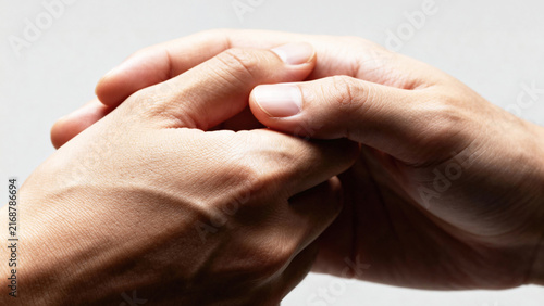Close-up of two human hands gently clasping each other against a neutral background, showcasing skin texture and details of fingers and nails