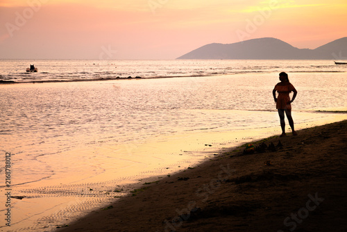 Silhouette of a person standing on the beach at sunset near calm waters