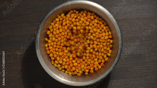 Top view of ripe orange sea buckthorn berries floating in water inside metal bowl on dark wooden background, close up. Concept of washing fresh autumn fruit harvest for tea, oil or healthy dessert