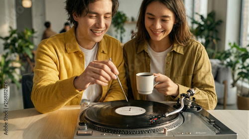 Modern morning music, two close friends in bright yellow shirts carefully placing a silver needle on a sleek minimalist turntable