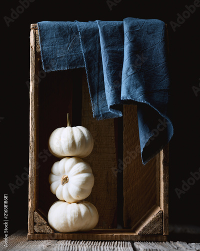 White decorative Baby Boo pumpkins in wooden box with blue napkin close up. Thanksgiving or Halloween food styling in cozy autumn setting