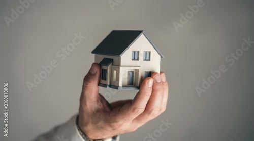 Hand holding an inverted miniature house model representing real estate market instability.