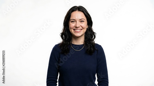 Smiling young woman with dark wavy hair wearing a navy sweater, standing against plain white studio background