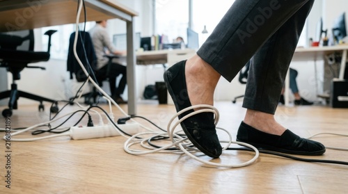 Person tripping over tangled electrical cables on office floor, workplace safety hazard.