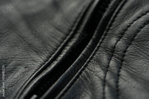 Black genuine leather biker jacket texture background Macro close-up of black genuine leather biker jacket texture with natural grain, wrinkles and stitched details. Dark leather surface creates a sty