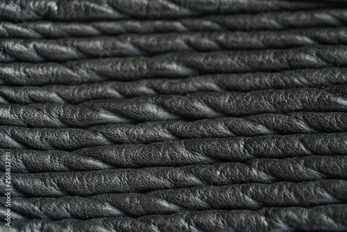 Black genuine leather biker jacket texture background Macro close-up of black genuine leather biker jacket texture with natural grain, wrinkles and stitched details. Dark leather surface creates a sty
