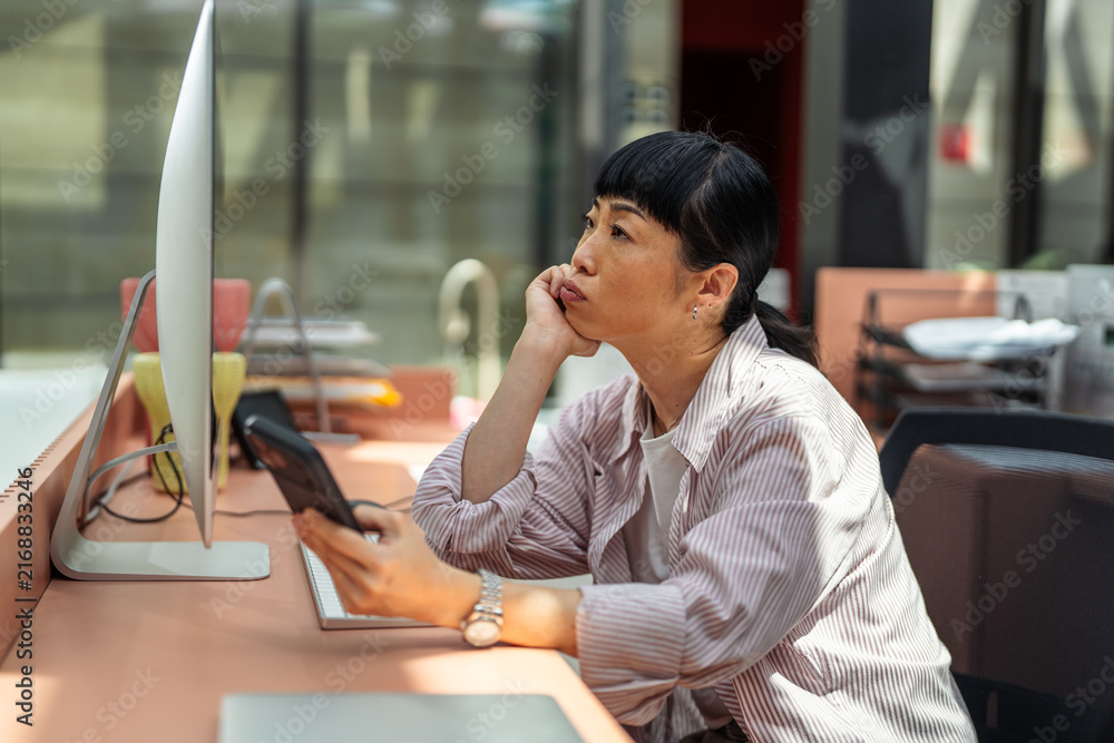 Obraz premium Bored woman procrastinating work using smartphone in office