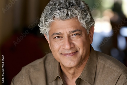 Close up portrait of a mature man with grey hair smiling warmly at the camera indoors