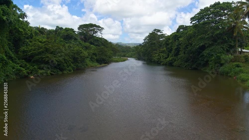 View of a river valley with trees along the banks. The river is surrounded by dense tropical forest. The sky is reflected in the water. Picturesque view of the calm river, refreshing bath.