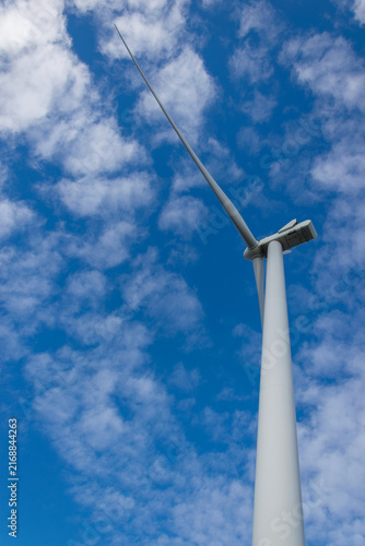 Wind turbine isolated against blue sky with white clouds looking up view low angle