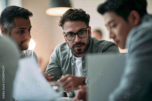 Diverse male colleagues discussing work strategies over documents and laptop in office