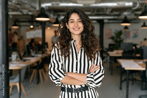 Smiling young businesswoman with curly hair standing with arms crossed in an open office