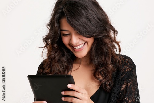 Smiling young woman with dark curly hair using a digital tablet against white background