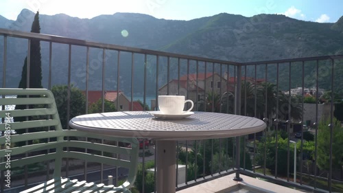 Woman’s hand placing a white cup on a table on a sunny summer balcony, cozy outdoor lifestyle and relaxing morning coffee concept