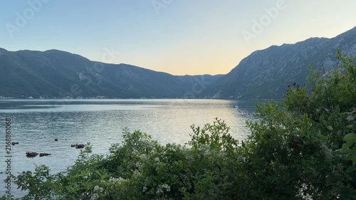 Scenic mountain bay at sunset, calm sea surrounded by dramatic peaks and warm golden evening light, peaceful coastal landscape