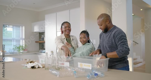 African family sorting recyclables at kitchen island, mother pointing to PAPER GLASS PLASTIC bins