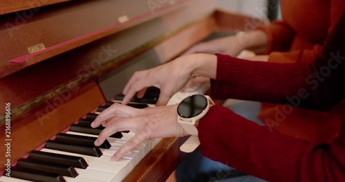 Fingers landing on keys are starting two pairs of hands playing duet on upright piano