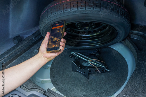 Auto expert taking photo of a car jack and tools in the trunk with a smartphone. Pre-purchase vehicle inspection report, checking equipment