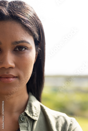 African American woman looking at camera in park wearing olive shirt, stud earring, copy space